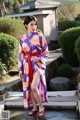 A woman in a purple and orange kimono standing next to a pond.