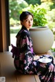 A woman in a kimono sitting on a window sill with a cup of tea.