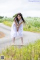 A woman in a white dress standing on the side of a road.