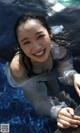 A young woman in a white shirt is smiling in a pool.