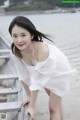 A woman in a white dress leaning on a wooden dock.