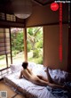 A naked woman laying on a bed in front of a window.