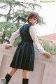 A woman in a school uniform leaning against a wall.