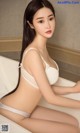 A woman in a white bra and panties sitting in a bathtub.