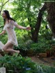 A woman in a white dress is dancing in the woods.