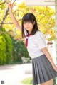 A woman in a school uniform holding a branch of a tree.