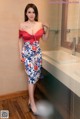 A woman in a red top and blue skirt posing in a bathroom.